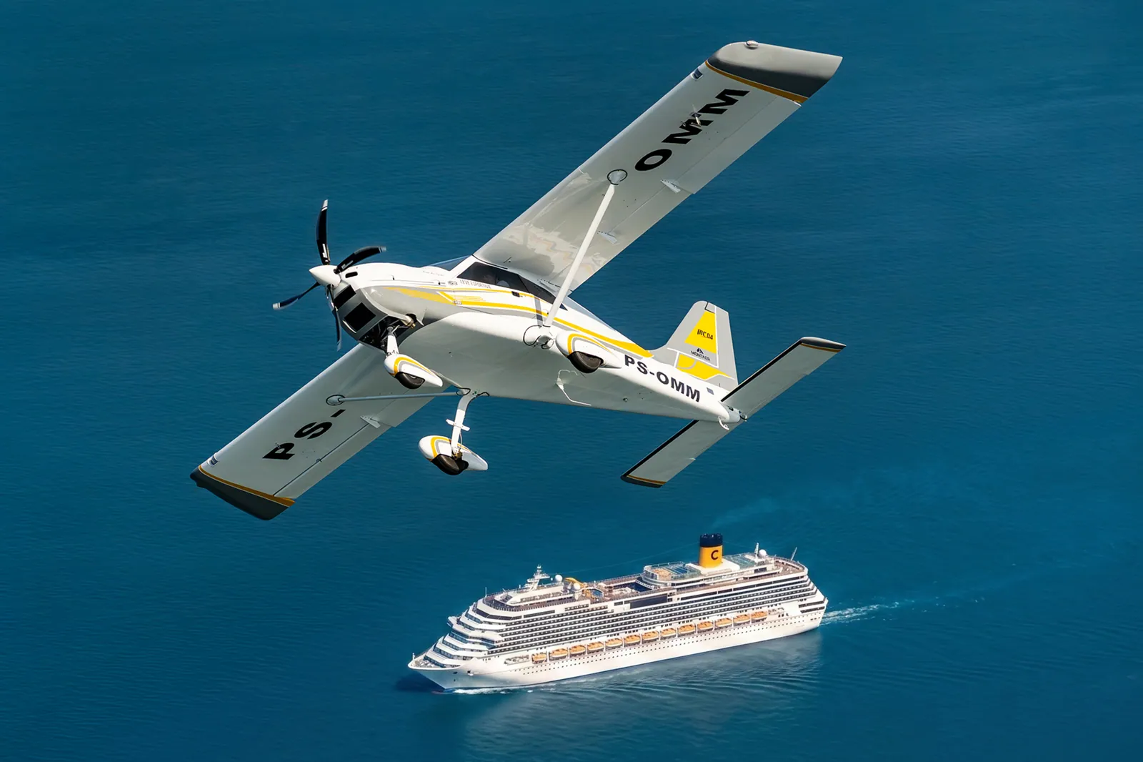 MC04 amarelo inclinado sobre o mar, com um navio de cruzeiro abaixo