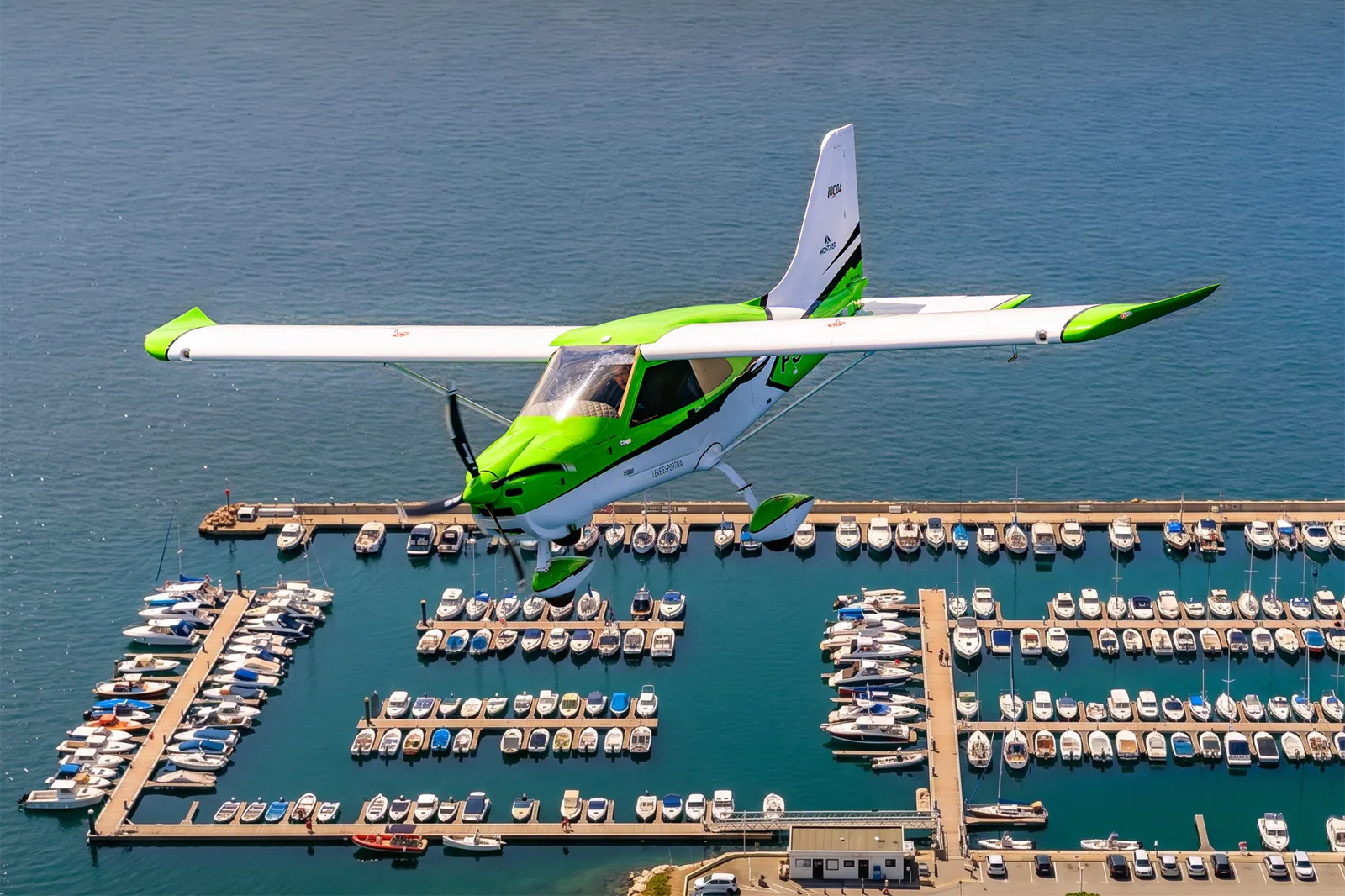 MC04 verde em voo sobre uma marina cheia de barcos
