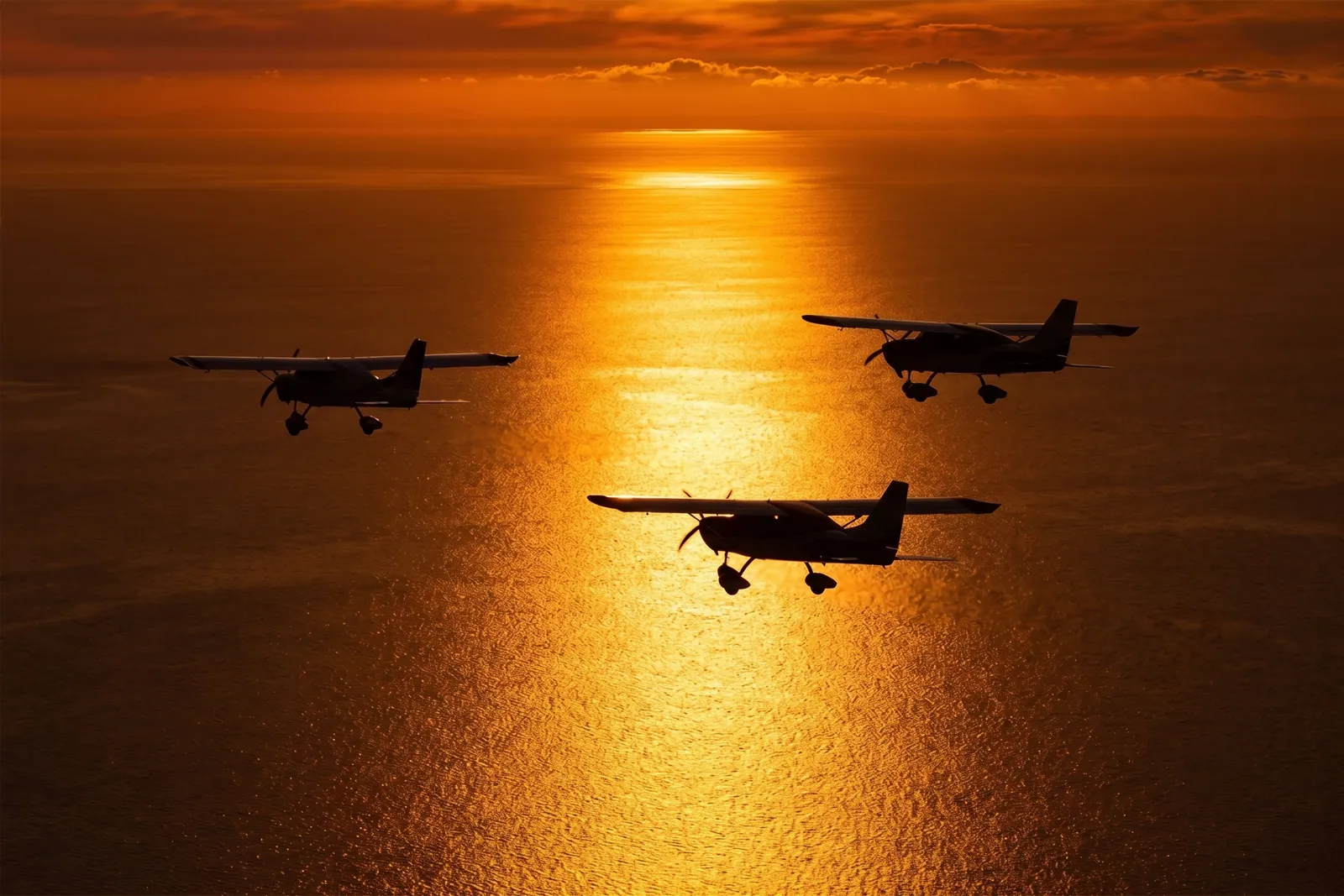 Silhuetas de três MC04 voando em formação sobre o mar ao pôr do sol